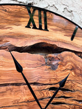 Olive wood wall clock with live edge wood slices set in black epoxy resin within a round black metal frame