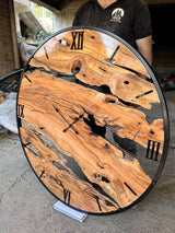 Large handmade olive wood wall clock photographed in the workshop, showing scale, natural voids, flowing grain and live edge construction