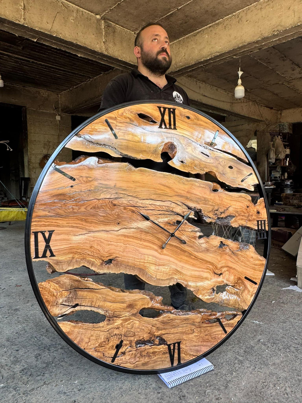 Front workshop view of the oversized olive wood wall clock with bold grain, knots and metal outer ring